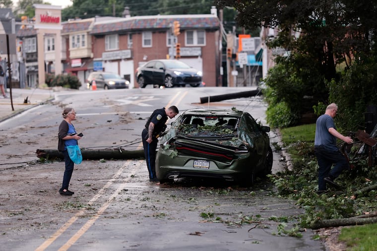 An Upper Darby policeman inspects a car that was crushed by a tree limb during last week's storm. 