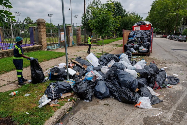 Workers pick up trash at a designated dump site load dumpsters at Columbia Avenue and 60th Street.