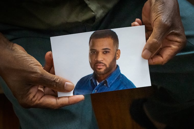 Jonah Wamah holds a photograph of his son, Joseph Wamah Jr., one of the victims in the mass shooting that took place in Kingsessing in July 2023.