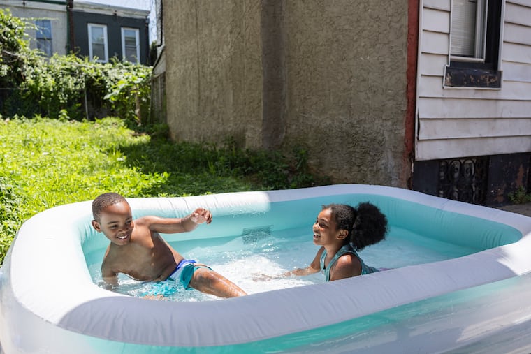 Neighbors Byron McDonald, 7, and Calii Wilson, 7, are cooling off in the summer heat in a pool outside their homes in Philadelphia on Tuesday.